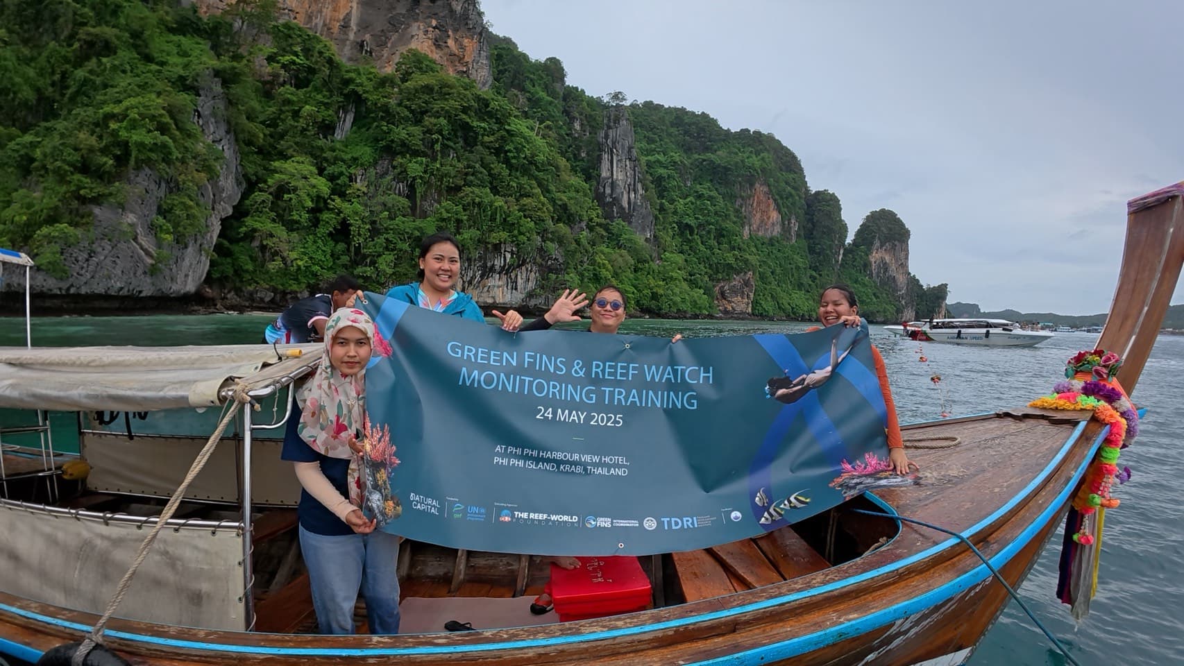 Barracudas crew holding the Green Fins and Reef Watch Monitoring Training banner on a longtail boat at Phi Phi Island